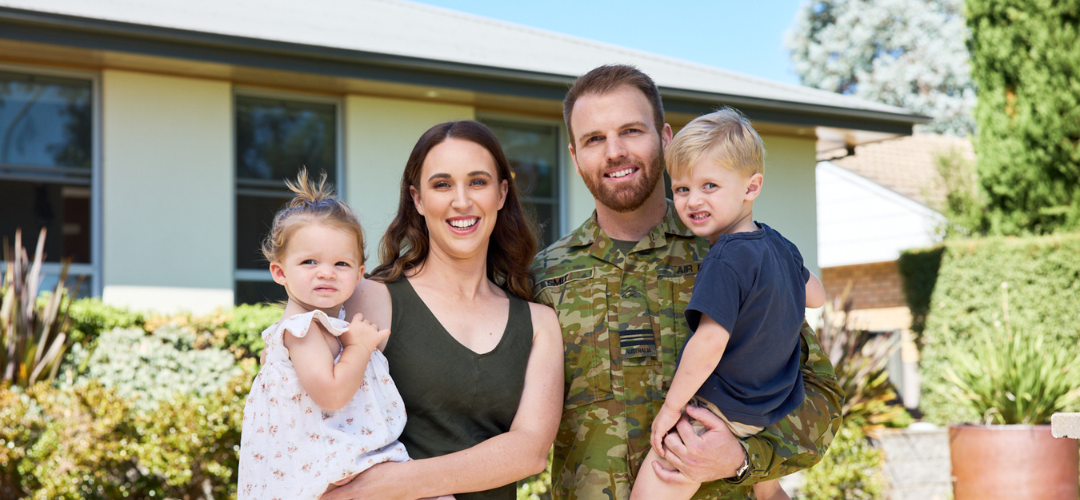 Defence member standing in front of house with family
