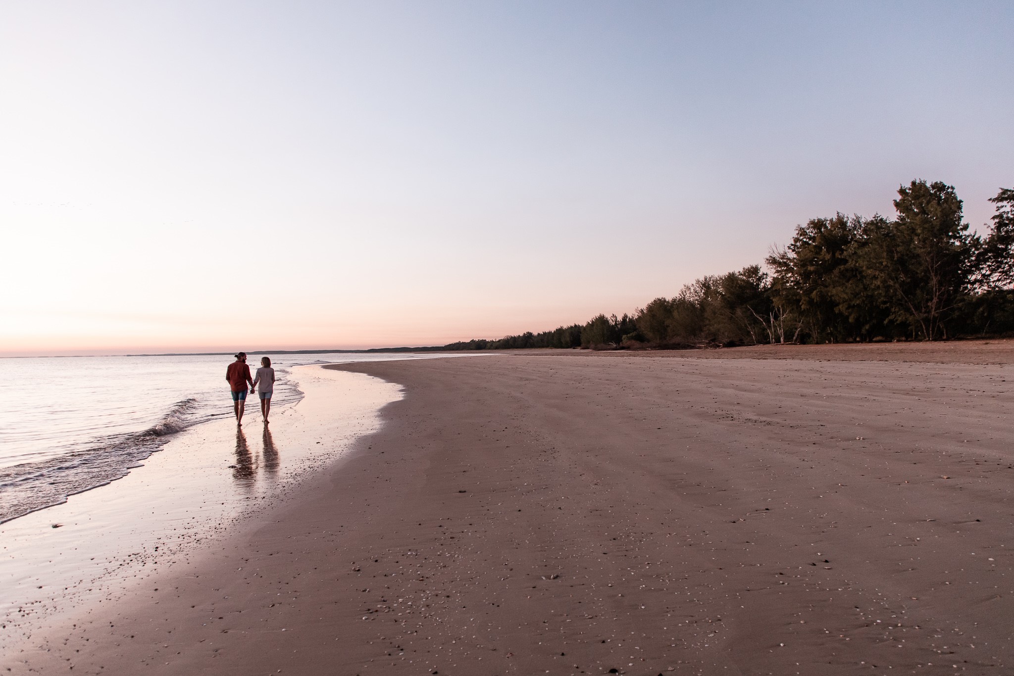 An image of a couple walking in the distance along a beach at sunset