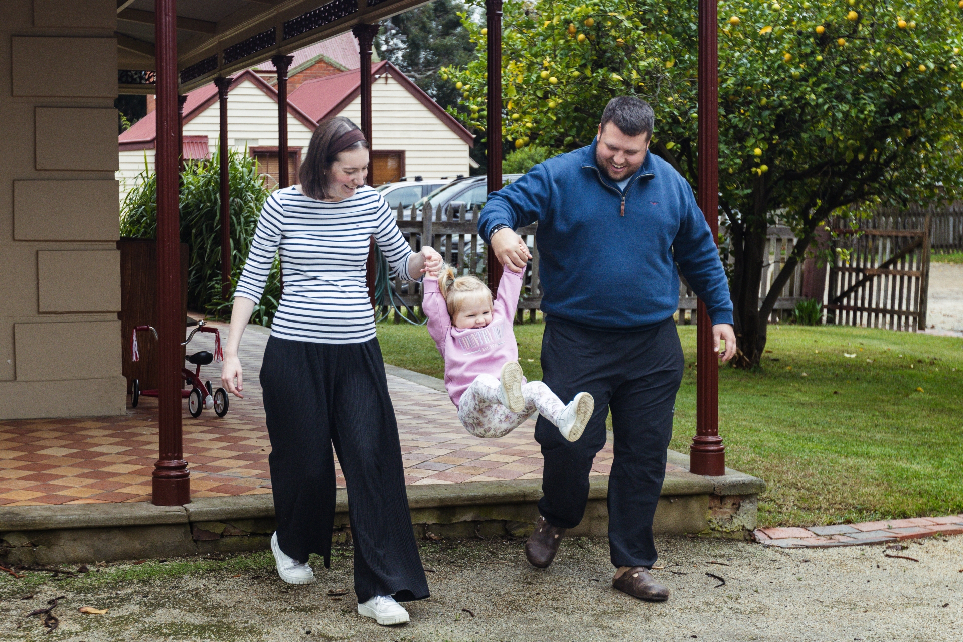 Woman and man each holding the hand of a young girl and swinging her off the step