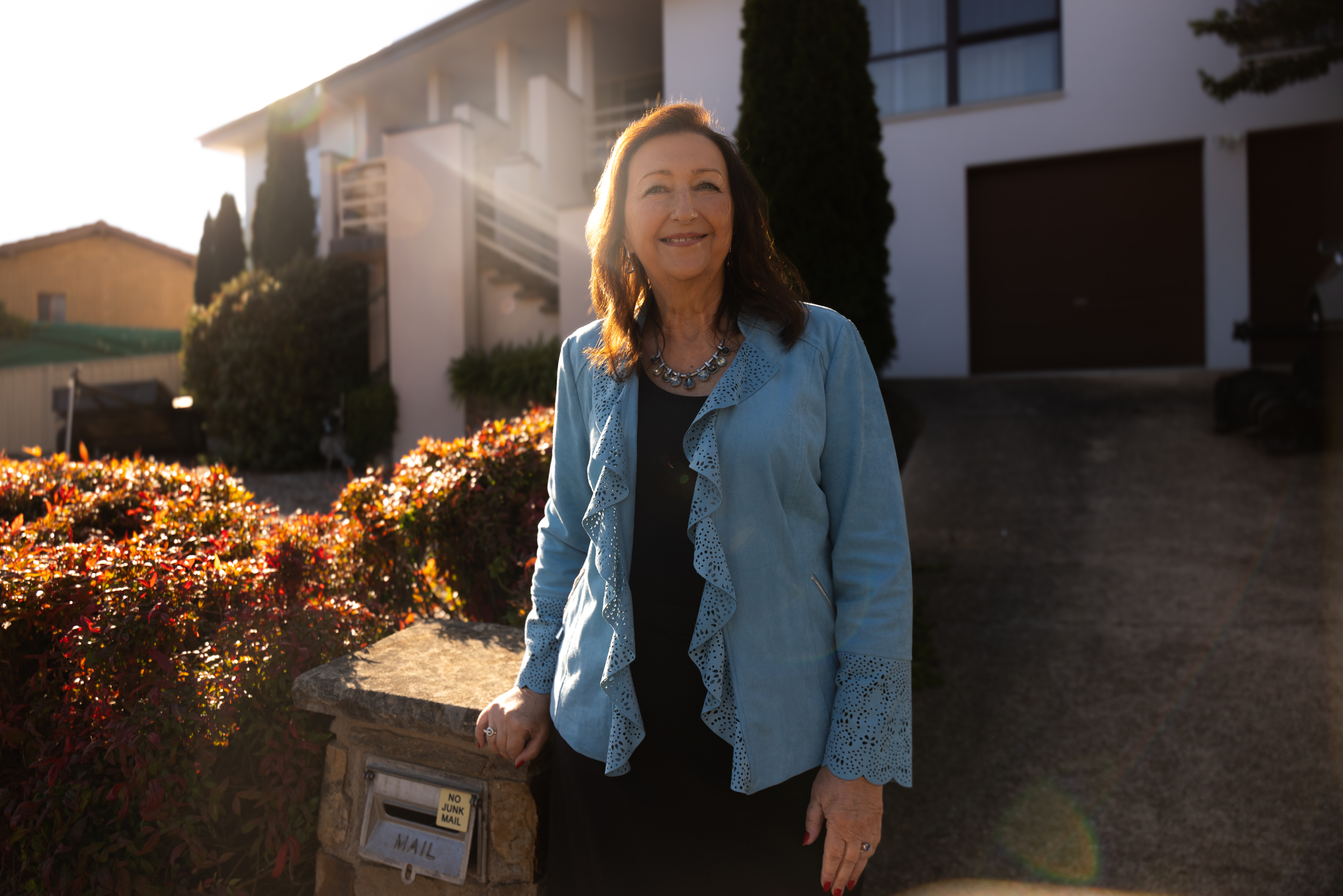 Person standing outside a house, with sunlight shining across the front garden.