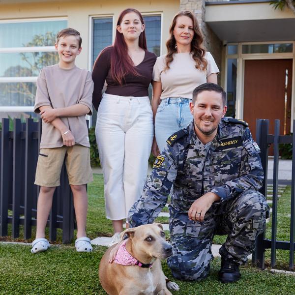 Family of four standing in front of their home with their pet dog.