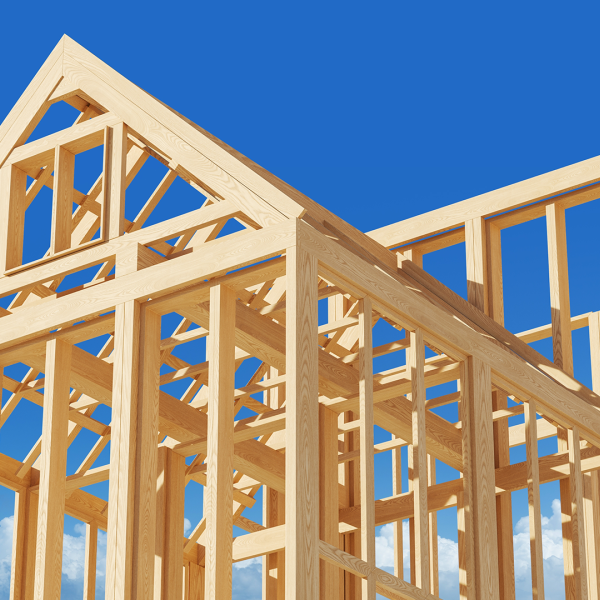 The timber frame structure of a house under construction against a clear blue sky.