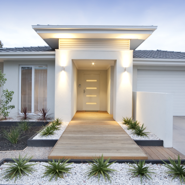 A modern white single-storey home with a timber deck walkway and contemporary landscaping at dusk.