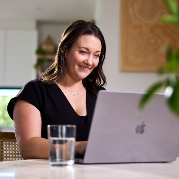 Smiling woman sitting at table working on a grey laptop