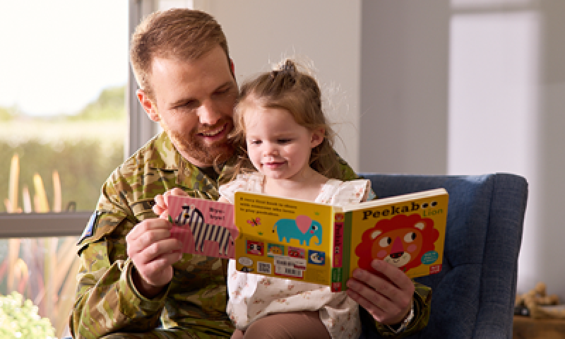 Defence member reading a picture book to his child.