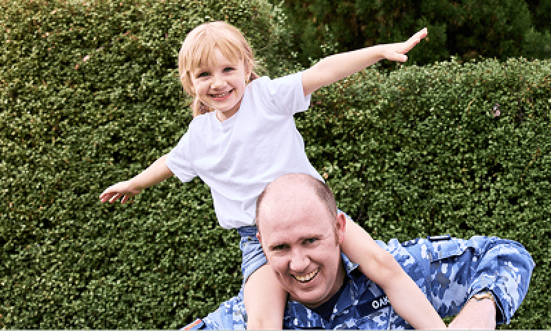 Defence member with young child on shoulders, both smiling. 