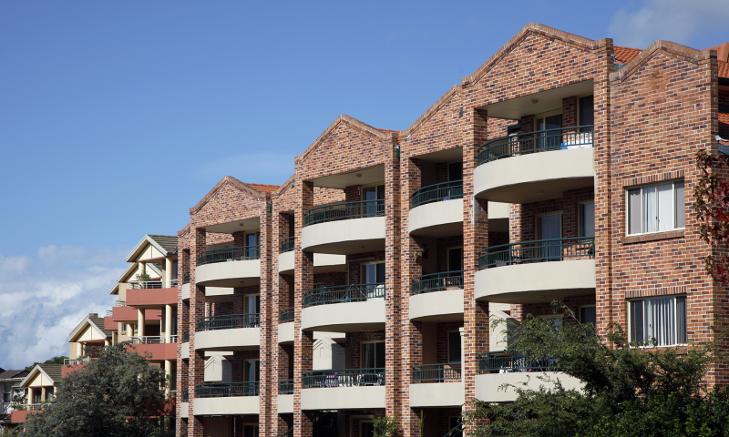 A multi-storey brick apartment complex with balconies under a clear blue sky.