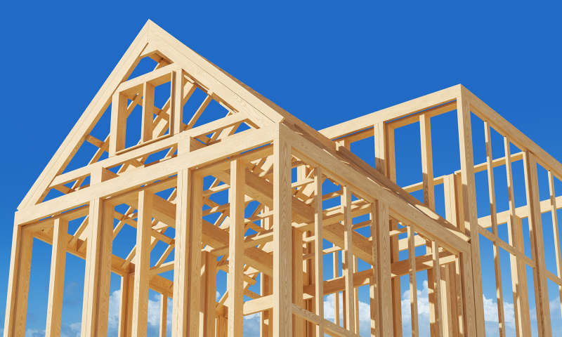 The timber frame structure of a house under construction against a clear blue sky.
