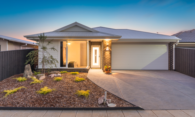 A modern single-storey brick home with a double garage, illuminated entrance, and landscaped front garden at dusk.