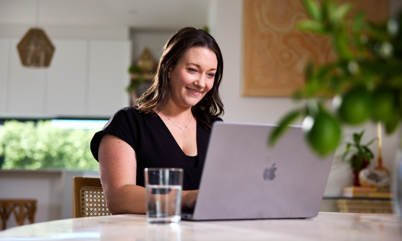 Smiling woman sitting at table working on a grey laptop