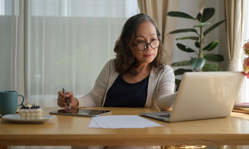 Senior mature woman is watching online webinar on laptop computer while remote working from home.