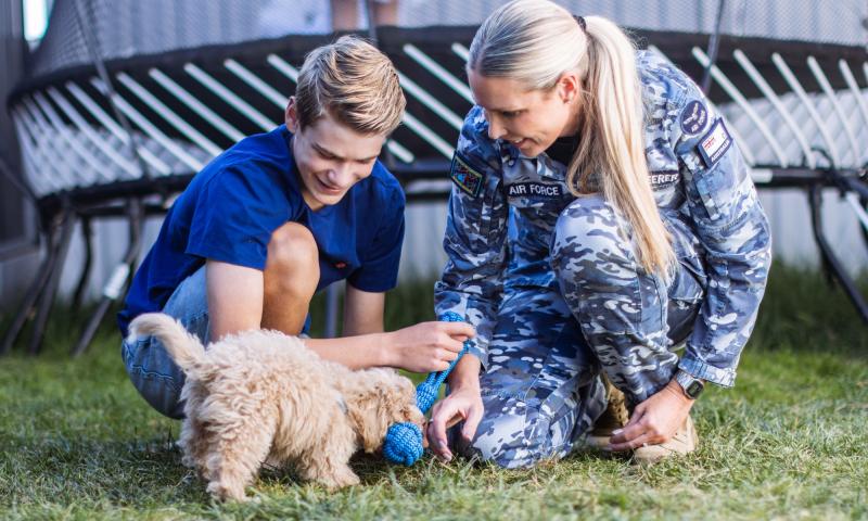 An Air Force Defence member plays with their child and dog outside.